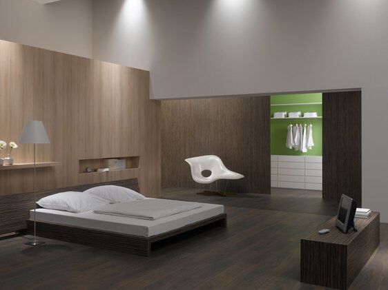 Schlafzimmerimpression mit Holzverkleidung an Wand Schlafzimmerimpression von Bett, Nachtisch und Sideboard mit Holzverkleidung an Wand und indirektert Beleuchtung